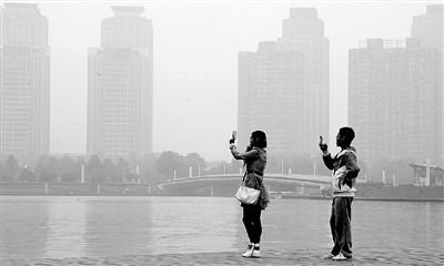 29日中午，鄭東新區(qū)如意湖畔，兩個(gè)年輕人拍攝霧霾中的景色。 鄭州晚報(bào)記者 馬健 圖